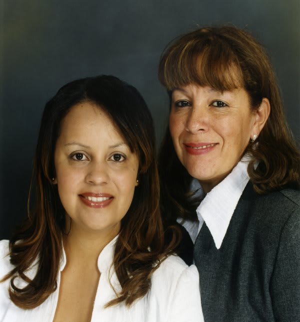 Two women posing together in a studio portrait, both smiling and dressed in formal attire.