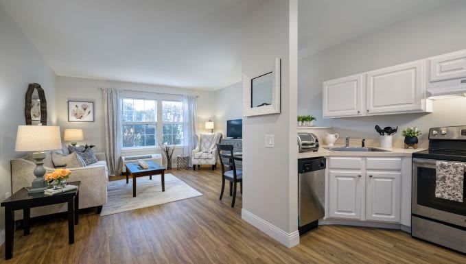 A modern apartment interior featuring a cozy living room with a connected kitchen area, highlighted by wood flooring and white cabinetry.