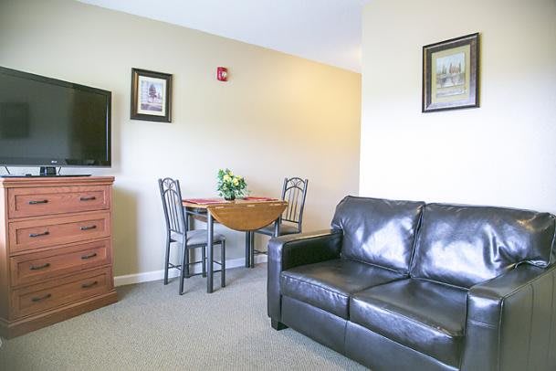A cozy living room with a black leather sofa, a small dining table with two chairs, and a television.