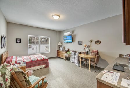 A cozy bedroom with a bed, chairs, and a wall-mounted television.