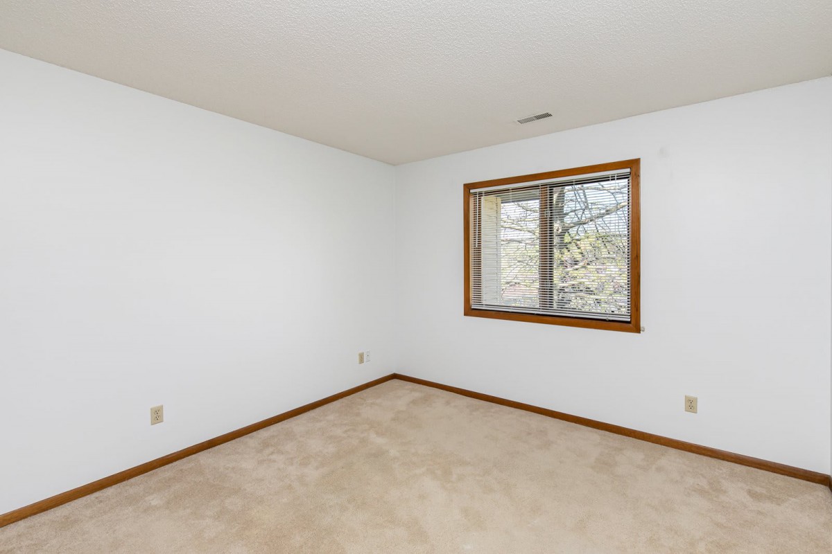 An empty room with white walls, carpet flooring, and a window with wooden trim.