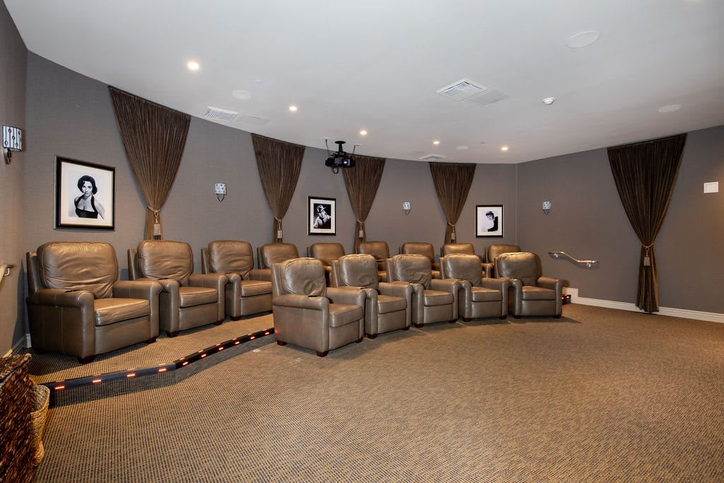 A cozy home theater room with a row of recliner chairs and a ceiling-mounted projector.