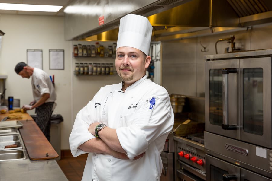 A chef stands confidently in a professional kitchen.