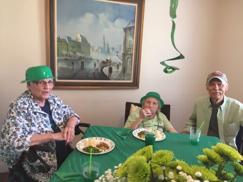 A group of elderly individuals celebrating with festive green decorations and hats for a St. Patrick's Day party.