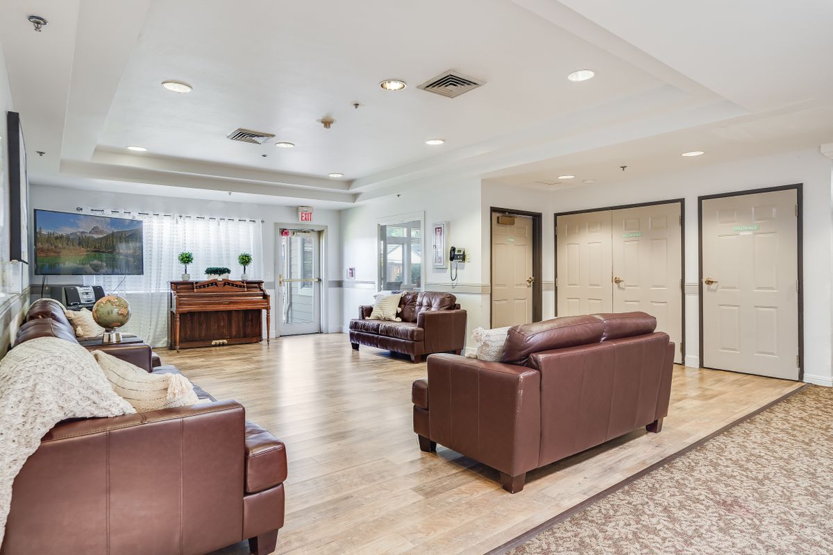 A spacious living area featuring leather sofas and a piano, with modern decor and wood flooring.
