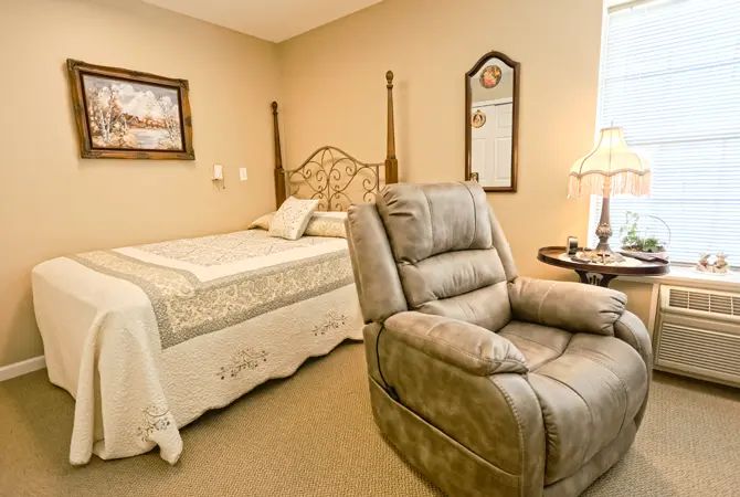 A cozy bedroom featuring a bed, reclining chair, and decorative elements like a mirror and lamp.