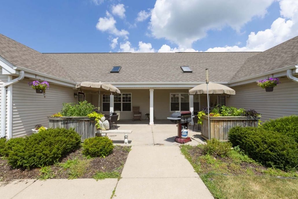 A residential house with a patio and garden, featuring outdoor umbrellas under a partly cloudy sky.