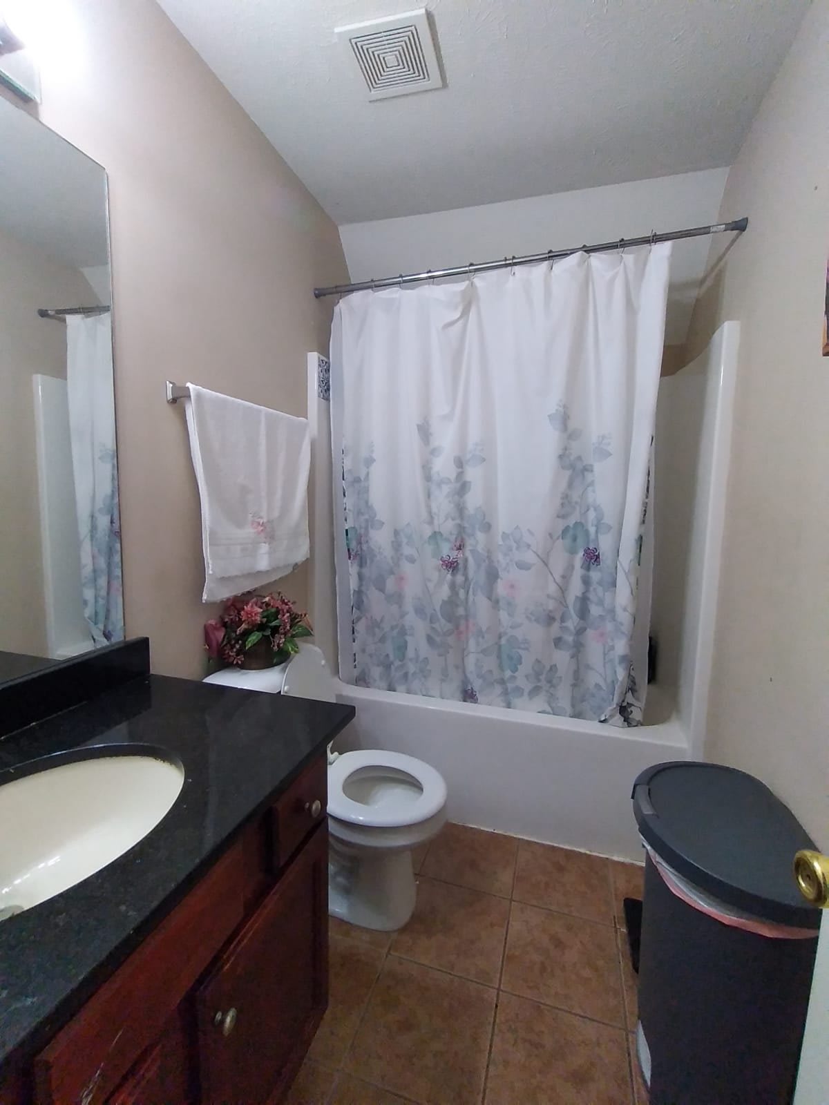 A modern bathroom with a countertop sink, toilet, and a shower/tub combination with a patterned curtain.