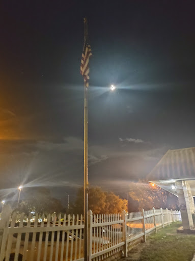 A night scene featuring a flag pole illuminated by artificial lights and the moon in the background.