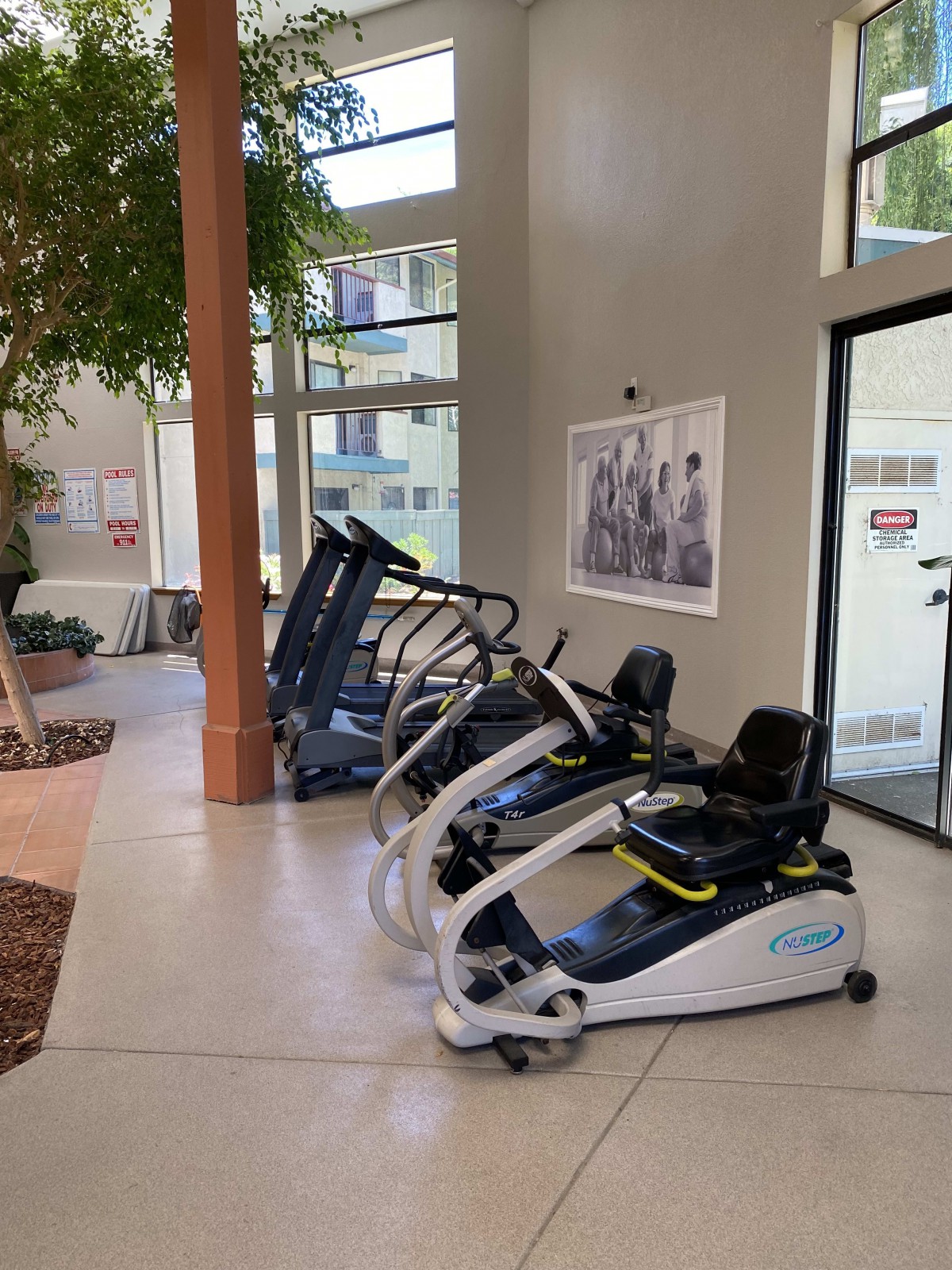 A fitness center with treadmills and stationary bikes lined up near large windows.