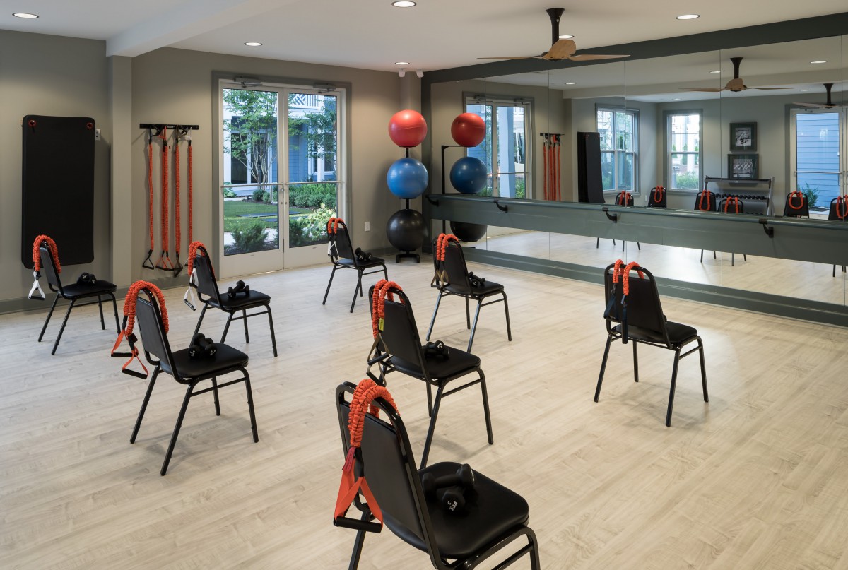 A spacious exercise room with chairs arranged for a workout session, featuring mirrors and fitness equipment.