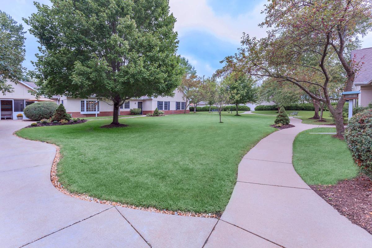 A landscaped outdoor area with a winding pathway, lawn, and trees in front of a building.