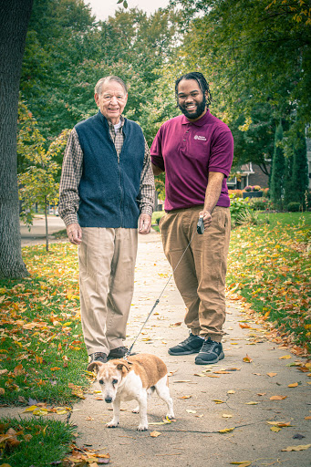 Two individuals enjoying a stroll with a dog on a picturesque autumn day.