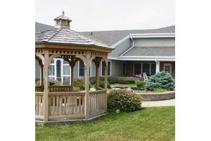A wooden gazebo in a landscaped yard next to a house.
