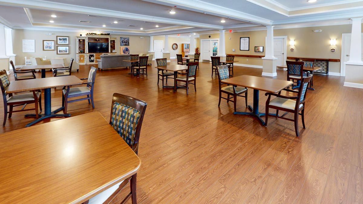 A spacious dining area with wooden flooring and neatly arranged tables and chairs.
