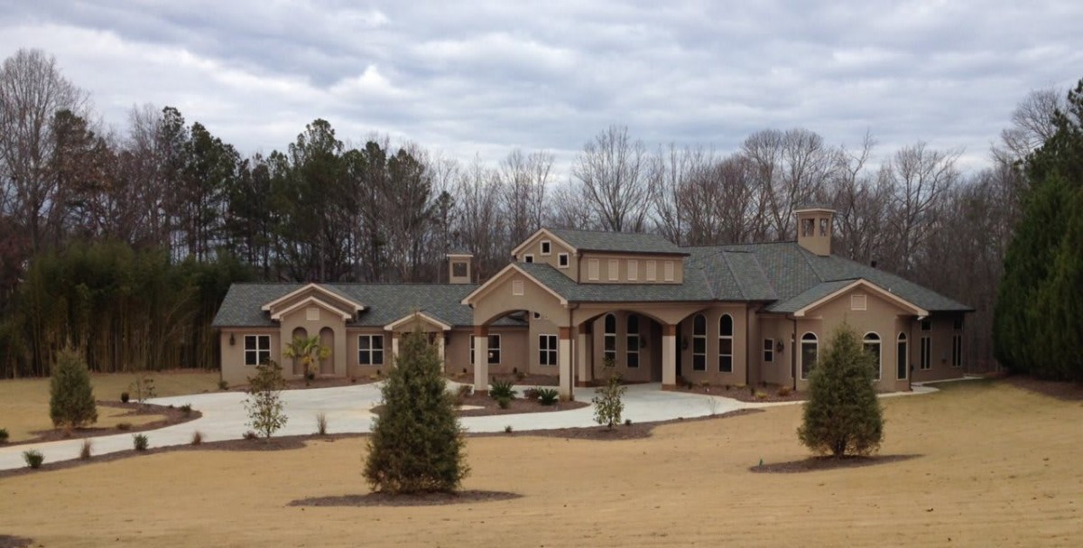 A large brick residential house with landscaped surroundings and a cloudy sky.