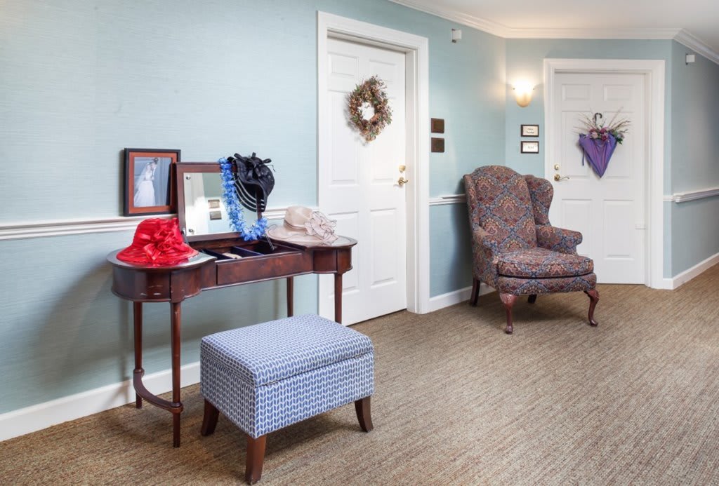 A cozy hallway featuring a decorative table with hats, an upholstered chair, and wreaths on the wall.