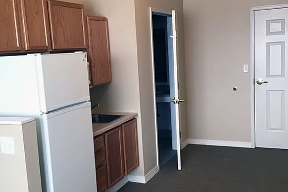 A compact kitchen area in an apartment, featuring a fridge, sink, cabinets, and an open doorway.