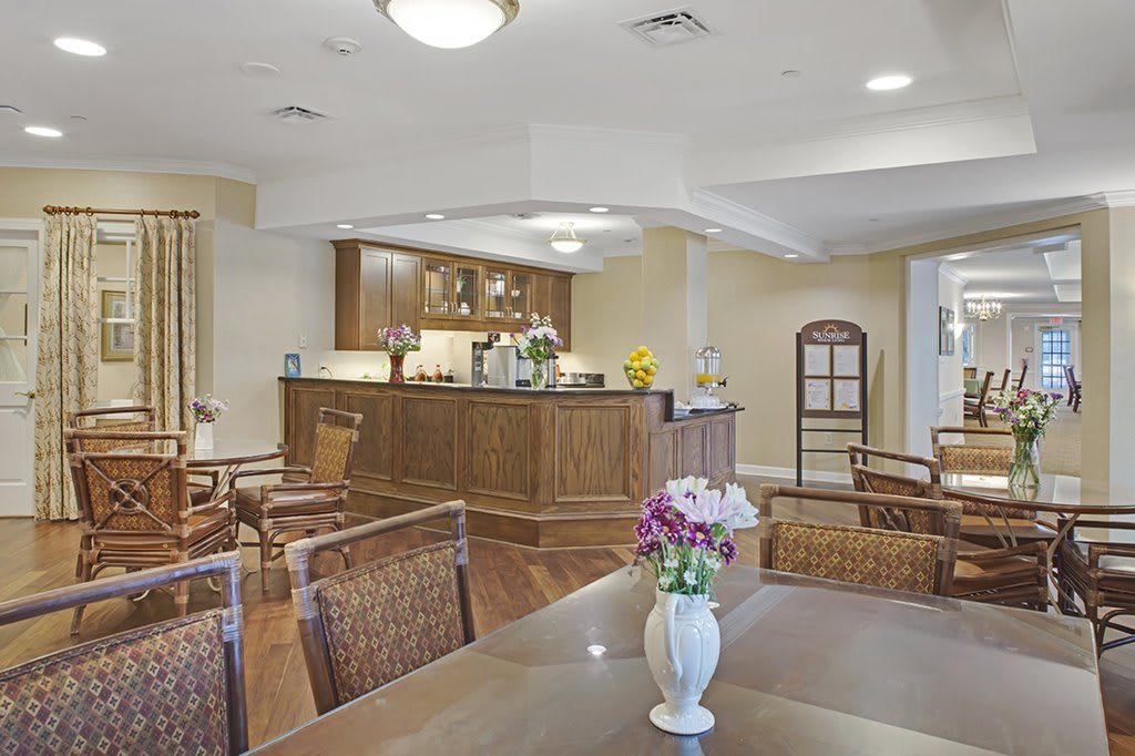 A cozy cafe interior with a wooden counter and comfortable seating, adorned with flowers.