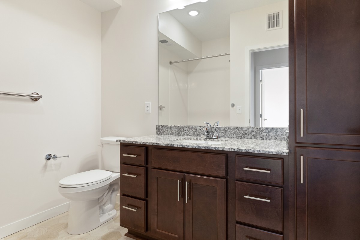 A modern bathroom featuring a dark wood vanity with a granite countertop and a large mirror.