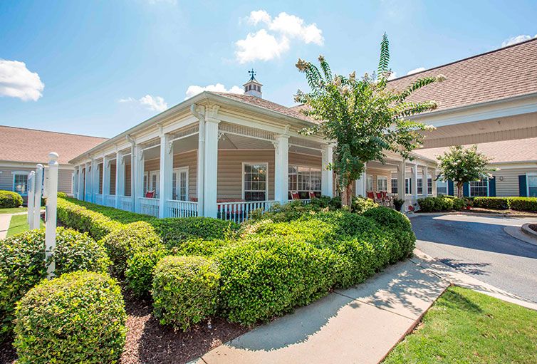 A well-maintained building with a large porch surrounded by lush green landscaping on a sunny day.