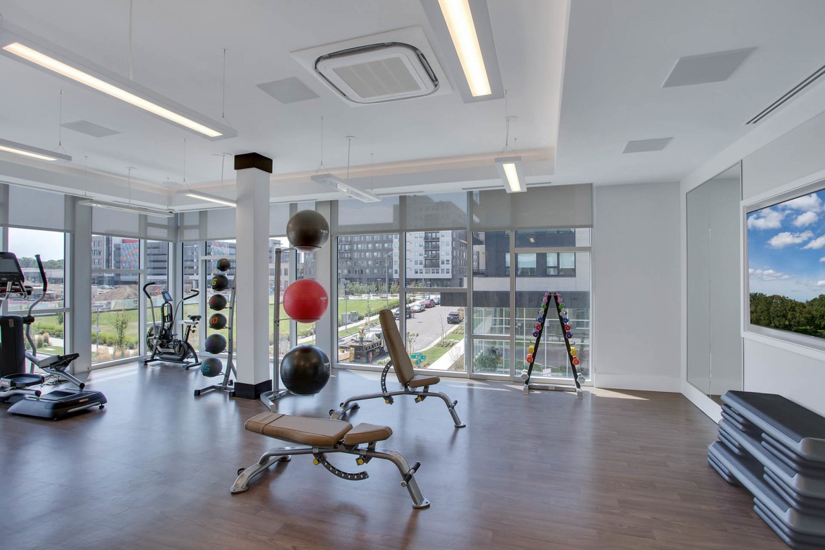 A modern gym with exercise equipment and weights, featuring large windows and a spacious workout area.