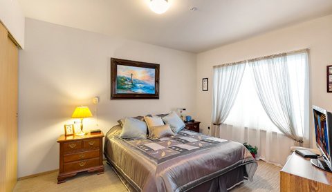 A cozy bedroom with a double bed, decorative pillows, bedside lamp, and a painting on the wall.