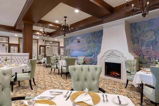A cozy and elegantly designed restaurant featuring comfortable green chairs, a warm fireplace, and artistic wall murals.