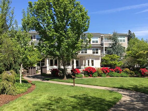 A scenic view of a residential building surrounded by lush greenery and vibrant flowers under a clear blue sky.
