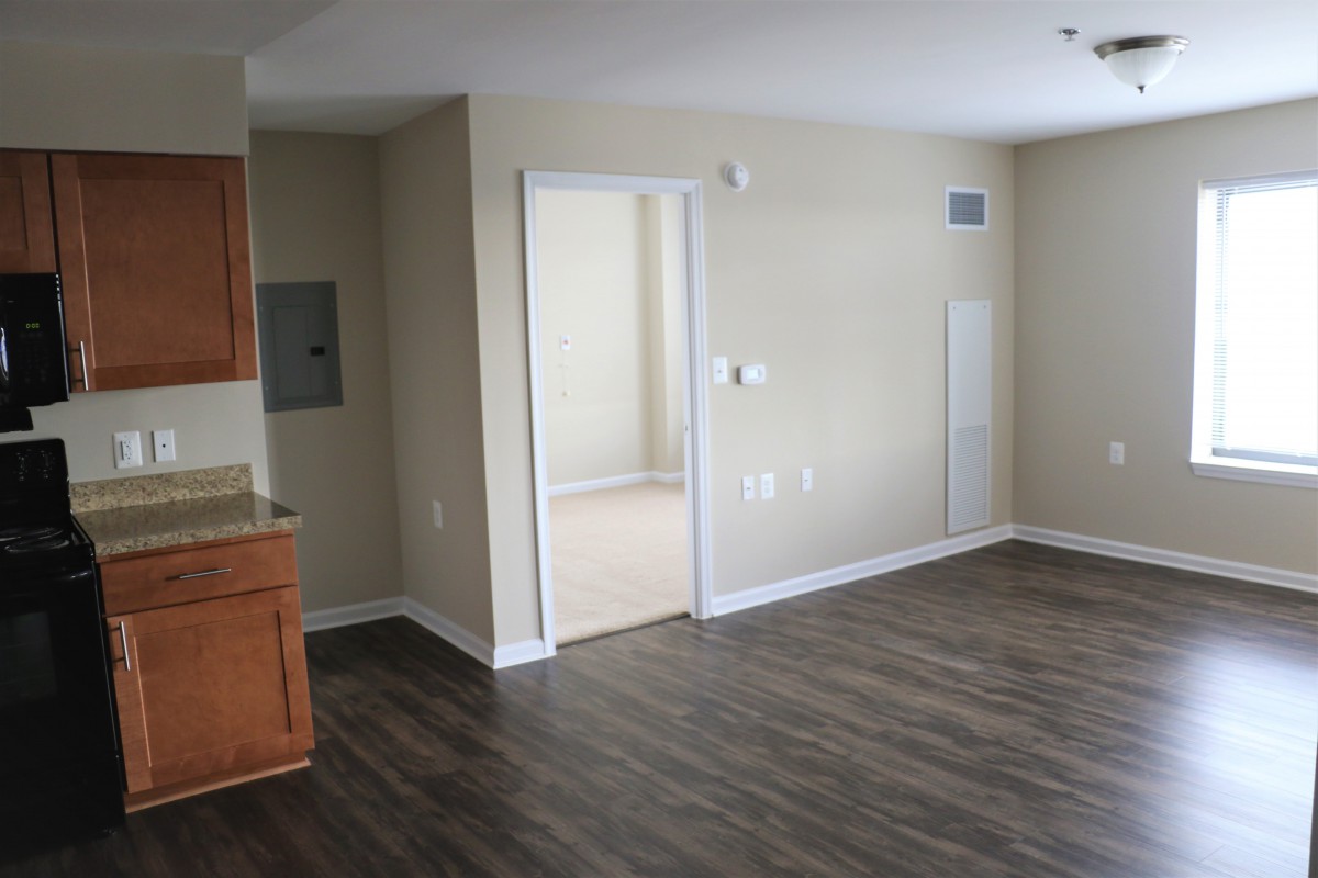 An empty apartment interior with wooden flooring and a view of the kitchen area.