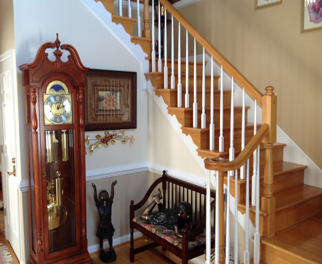 A home interior featuring a wooden staircase, a classic grandfather clock, and a decorative bench.