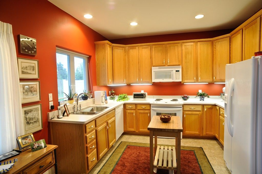 A modern kitchen with wooden cabinets and red walls, featuring a centered island and various appliances.
