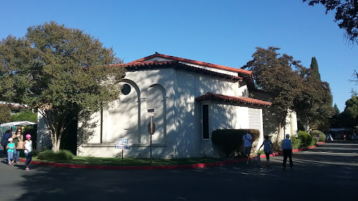 A unique architectural structure with a red-tiled roof, surrounded by trees under clear blue skies.