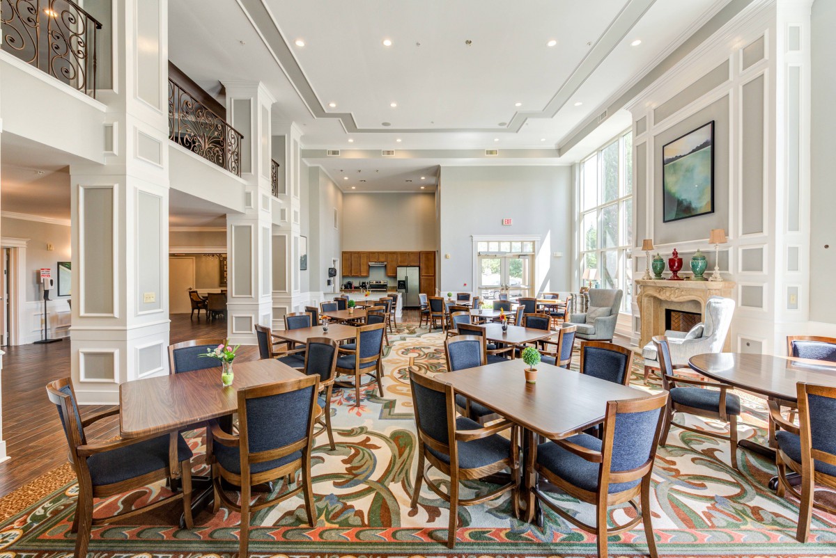 A spacious dining area with multiple tables and chairs, featuring large windows and bright lighting.