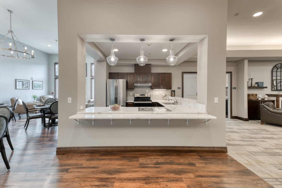 A modern kitchen with sleek appliances, a spacious white countertop, and stylish pendant lighting over a wood floor.