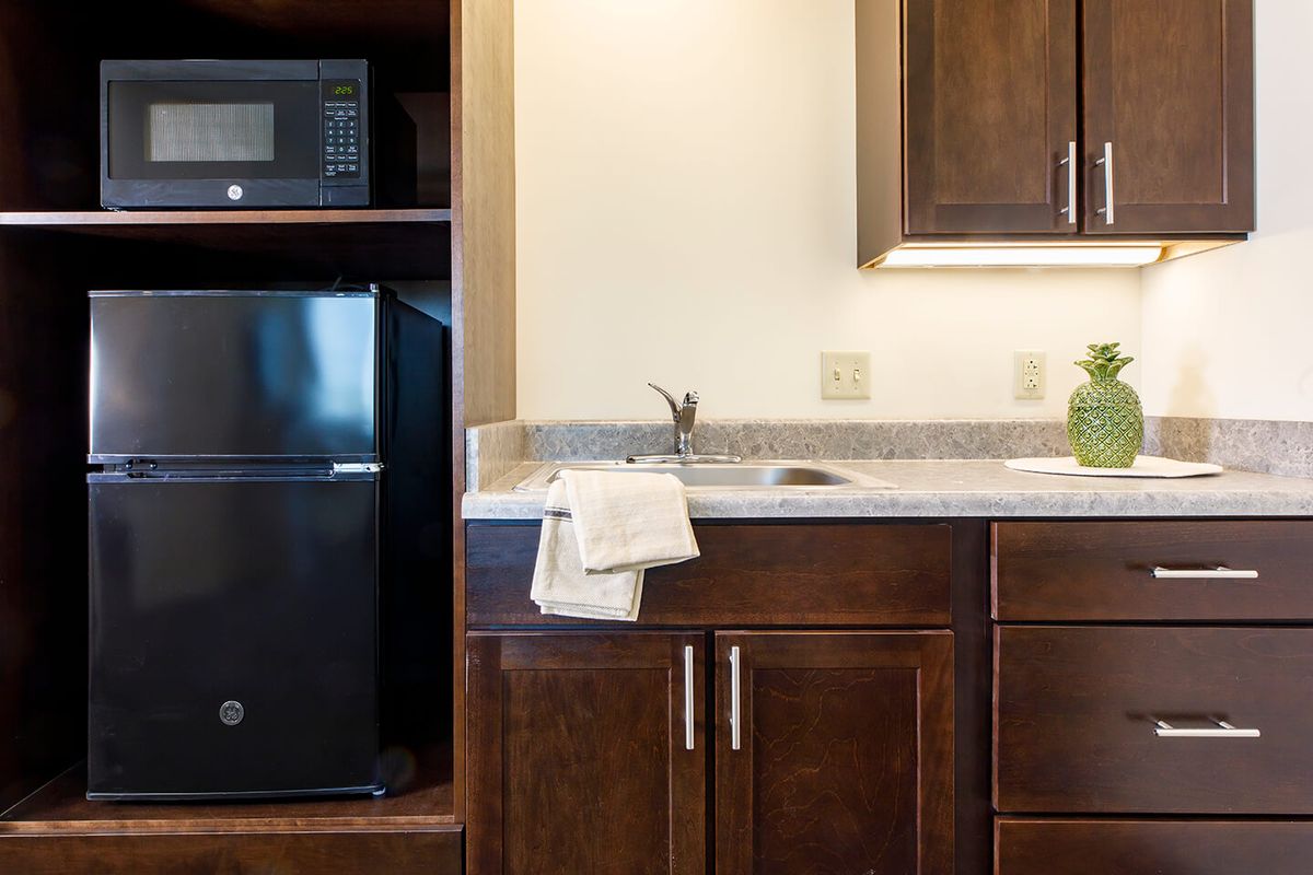 A compact kitchen area with a microwave, mini fridge, and wooden cabinets.