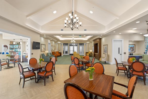 A spacious and elegantly decorated dining area with multiple tables and chairs, featuring a central chandelier.