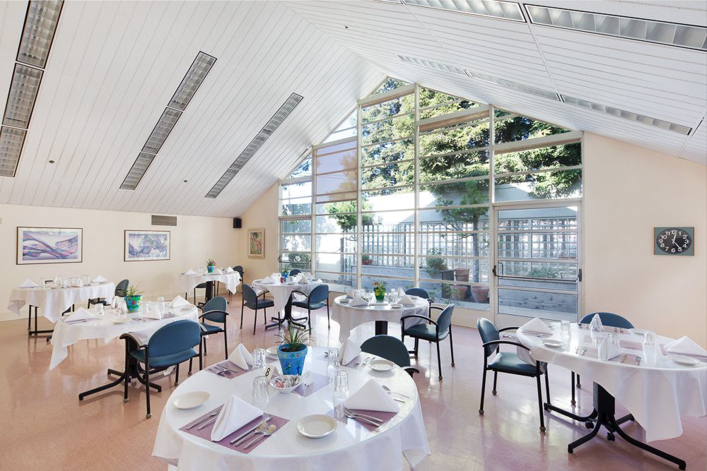 A bright and airy dining area with neatly arranged tables and chairs, featuring large windows that allow natural light to fill the space.