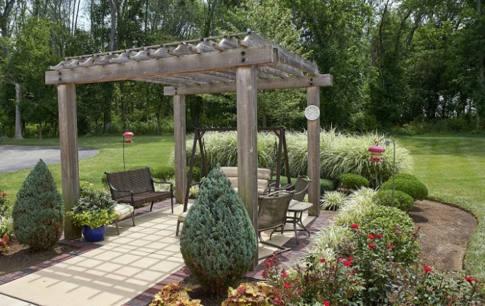 A beautiful garden featuring a wooden pergola with outdoor seating surrounded by lush greenery.