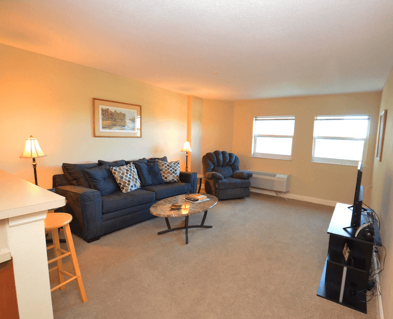 A cozy living room with a sofa, armchair, and coffee table, complemented by natural light from the windows.