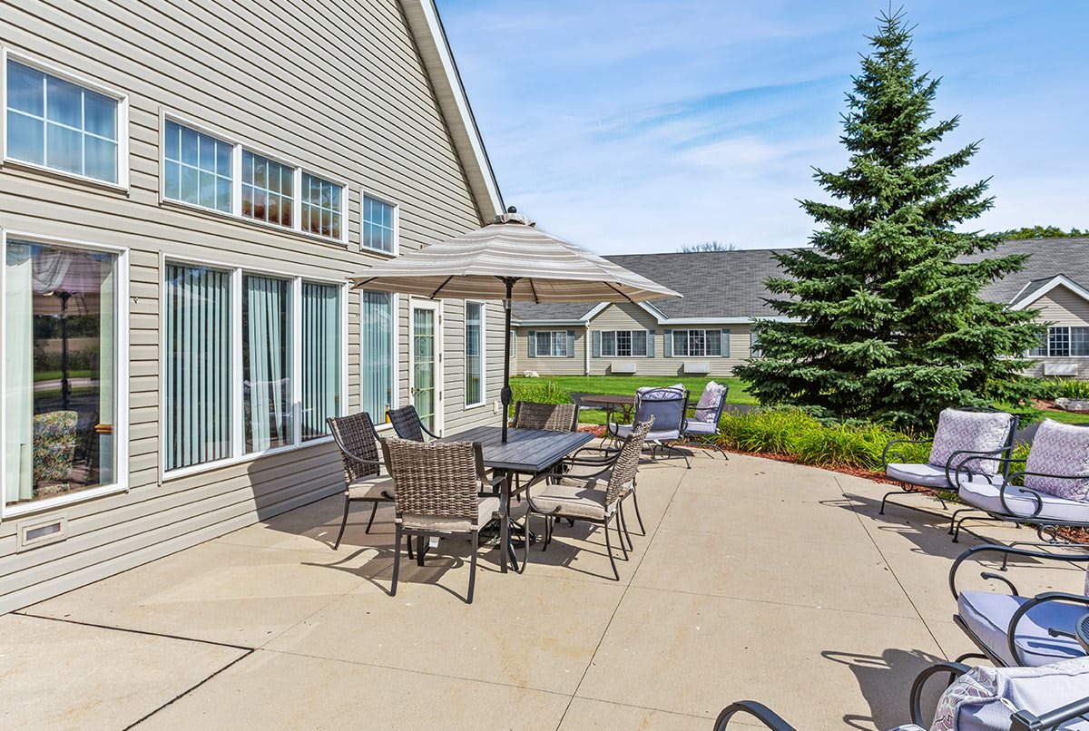A sunny patio with tables and chairs set up for outdoor dining, adjacent to a residential building and garden.