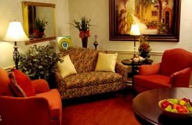 A cozy living room with a patterned sofa, two red chairs, and decorative elements such as a lamp, painting, and plants.