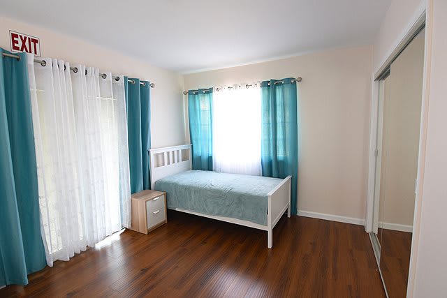 A minimalist bedroom with a daybed and teal curtains letting in natural light.