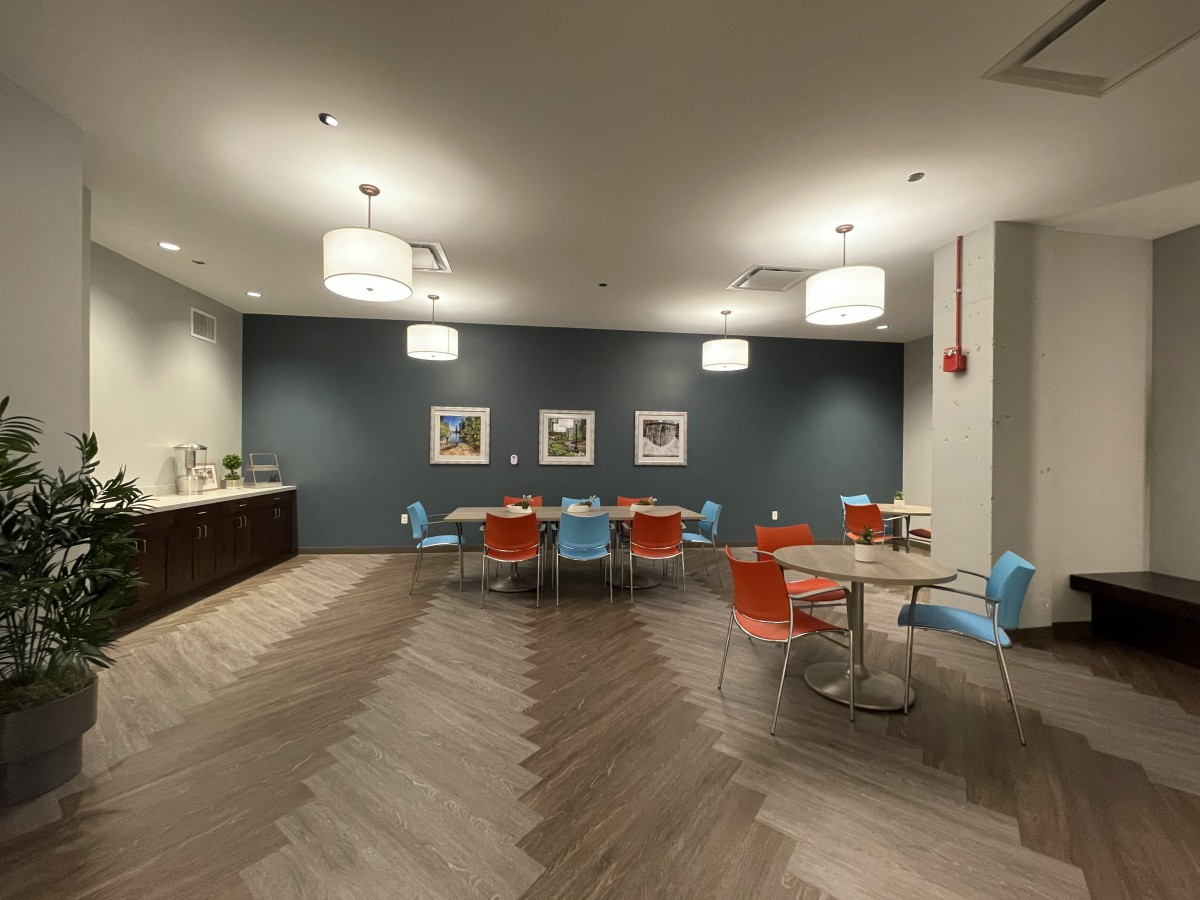 A modern office break room with colorful chairs and tables under warm lighting.