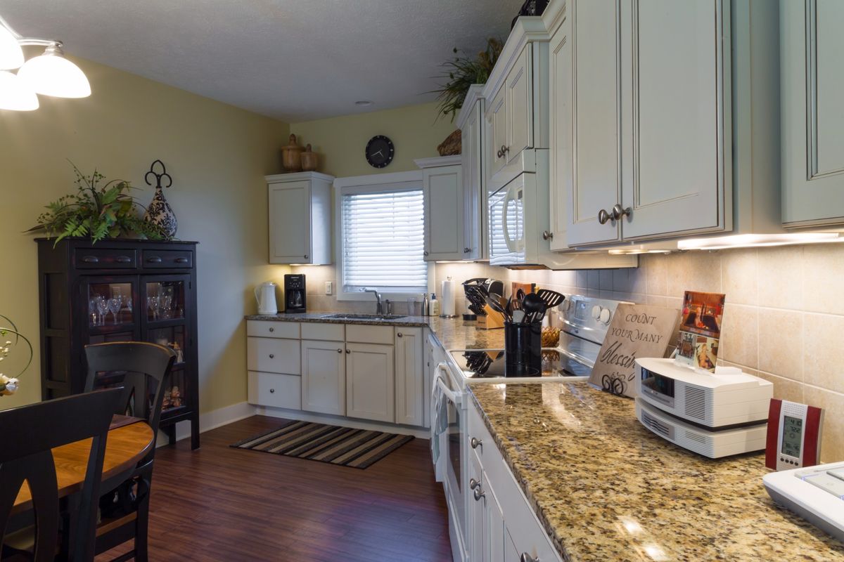 A modern kitchen with white cabinets and granite countertops, featuring a hardwood floor and various appliances.
