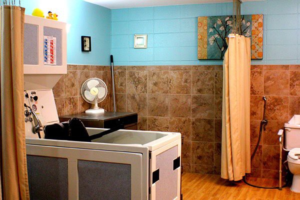 A cozy and organized laundry room featuring a washing machine, a small fan on a counter, tiled walls, and a curtain for separation.