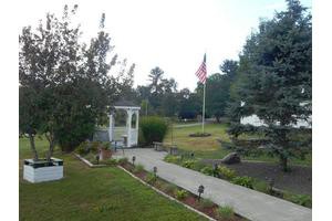 A serene outdoor garden with a pathway, gazebo, and flag surrounded by trees.