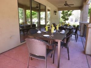 A patio dining area with a table set for a meal, surrounded by chairs and reflecting windows.