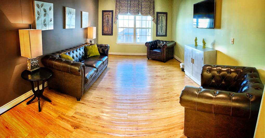 A cozy living room with leather sofas and a large window, featuring hardwood floors and decorative wall art.