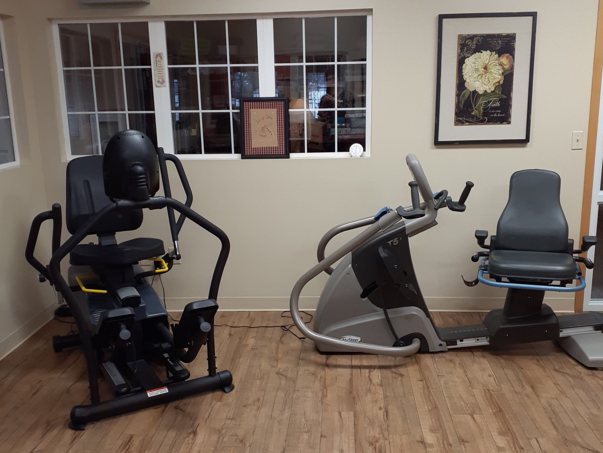 A fitness room featuring various exercise machines, including a recumbent bike and an elliptical trainer.